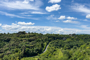 aerial view of a winding road through dense green forest hills under a blue sky with scattered clouds, featuring a