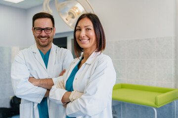 Confident Male and Female Doctors Smiling in a Bright Hospital Room Wearing White Coats