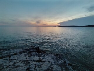 Obraz premium Peaceful Sunset Over the Sea with Rocky Shoreline and Calm Horizon