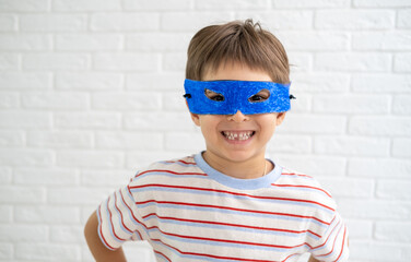 Cheerful strong little boy is wearing blue handmade mask like superhero playing at home.