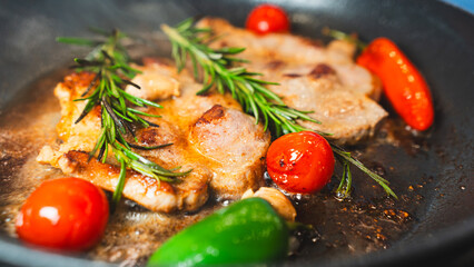 Juicy pork steak searing in cast iron pan with cherry tomatoes, rosemary and chili. Cooking process...