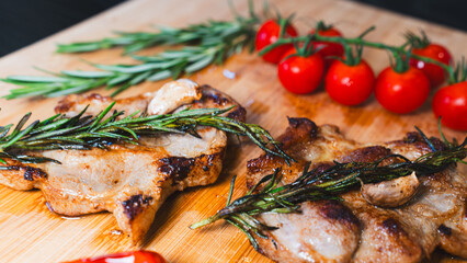 Perfectly grilled pork steak with charred edges and juicy interior, served on wooden board with cherry tomatoes, rosemary, chili and onions. Rustic meat photography