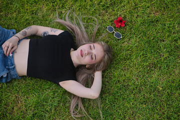 Young woman, beautiful, blonde, eyes closed, relaxed and calm, viewed from above, lying on green grass. Concept of relaxation, peace, spring, grass.