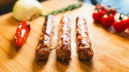 Juicy roasted pork sausage with perfect golden crust, served on wooden board with cherry tomatoes, rosemary, chili and onions. Rustic food photography