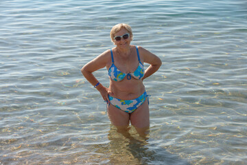 Elderly lady is standing in shallow water at sea beach.