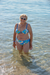 Elderly lady is standing in shallow water at sea beach.