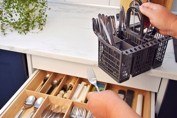 A woman puts cutlery into drawers after the dishwasher.