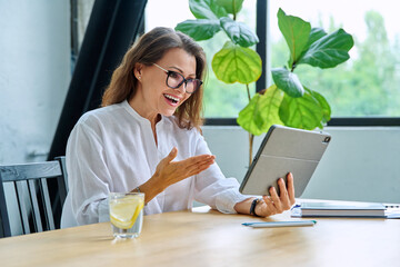 Middle aged female teacher entrepreneur using digital tablet for video online meeting
