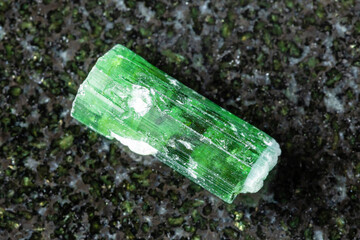 sample of rough verdelite crystal on black granite