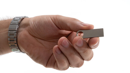 Person holding a metallic USB flash drive in hand against a white background during daylight