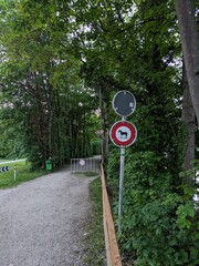 Naklejka premium Pathway in a lush green environment with traffic signs indicating restrictions. Ideal for concepts of nature, outdoor activities, or rural settings.