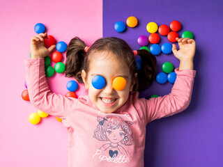 Petite fille qui s'amuse souriant les bras levés avec jetons multicolores sur fond rose et violet