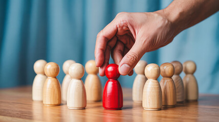 Hand selects a distinct red figure from a group of wooden people, symbolizing leadership and uniqueness.