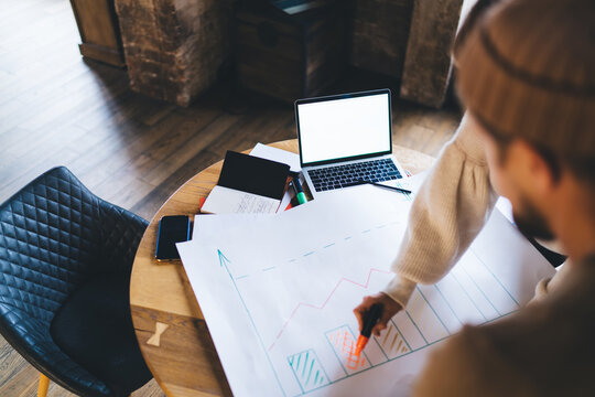 Freelancer woman outlines growth bars with marker while male partner analyzes graph, building strategic vision using paper sketch and laptop in modern digital planning workspace.