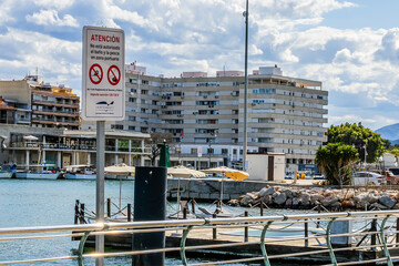 Warning sign with port and building in the background under cloudy sky in Gandia, Spain	
