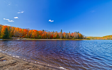Bright beautiful day with a low hanging cloud on top of the lake surrounded by fall foliage.