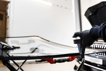 Applying adhesive to a car windshield using a caulking gun. Urethane caulking gun applies flexible adhesive, forming a watertight seal at car windshield replacement.