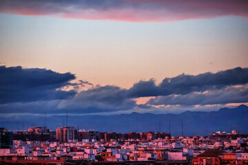 Various houses in a Spanish town with mountains on the horizon under a blue sky	
