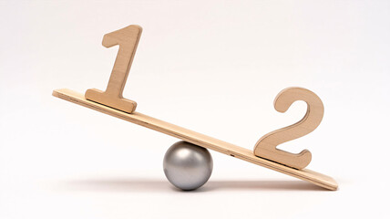 Wooden numbers one and two on a balanced seesaw symbolize disparity and comparison