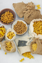 Pasta. Various kinds of uncooked pasta and noodles over light stone background. Traditional Italian