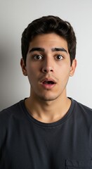 Obraz premium Astonished Young Man: A close-up portrait of a young man with wide, expressive eyes and an open mouth, conveying a look of utter surprise and disbelief.