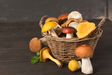 Wicker basket with variety of fresh mushrooms on wooden table
