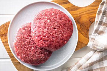 Raw burger beef patties on plate on white table. Top view.
