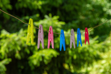 Close-up of colorful clothespins on a clothesline with blurred green trees in background. Bright outdoor detail for summer or home scenes. 