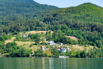 Turquoise water of Perucac Lake with green hills and rural houses on the opposite shore in Bosnia and Herzegovina. Tara National Park. Tara, Serbia.

