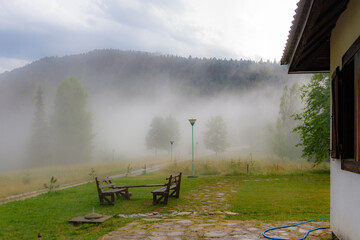 Misty forest and foothills in Predov Krst with wooden table and benches, and a walking silhouette. Tara National Park. Tara, Serbia.

