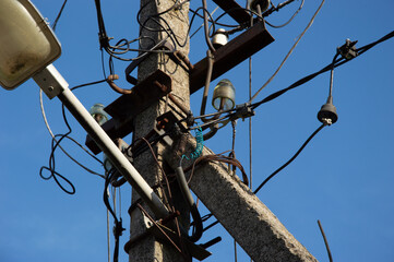 Utility pole showcases tangled wires and street light against a vibrant blue sky during the day,...