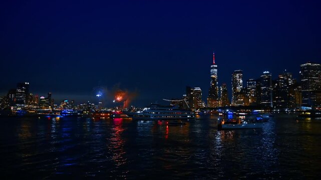 Beautiful night skyline of modern New York, USA with fireworks flashes. Numerous boats are watching the show on the river.