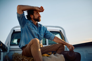 Exhausted farmer relaxing in back of truck after harvest in field.