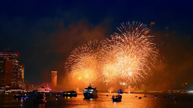 Fascinating firework show over the river waterscape. Multiple diverse boats are on the waterscape colored by the flashes. New York city celebration.