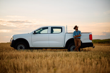 Full length of confident farmer with white pick-up truck in field.