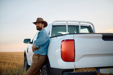 Confident farmer by his pick-up truck in harvested field looking away.