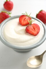 Delicious yogurt in bowl, strawberries and spoon on white table, closeup