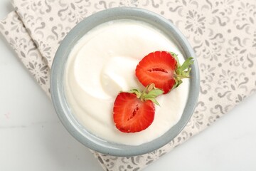 Delicious yogurt in bowl and strawberries on white marble table, top view