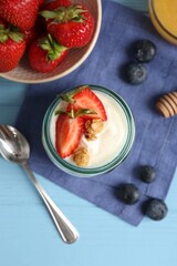 Tasty yogurt with granola, berries and spoon on light blue wooden table, flat lay