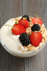 Tasty yogurt with granola and berries in bowl on wooden table, closeup