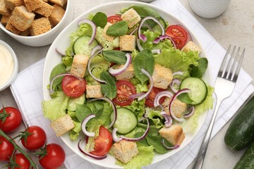 Delicious salad with croutons and vegetables served on light grey table, flat lay