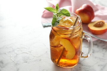 Refreshing iced peach tea with mint in mason jar on white marble table, closeup. Space for text