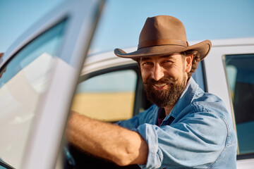Happy farm worker getting out of truck while arriving at field and looking at camera.