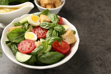 Tasty salad with croutons, tomatoes, cucumbers and basil on black table, closeup. Space for text