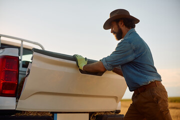 Farm worker closing back of his pick-up truck while working in field.
