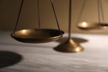 Scales of justice on wooden table against beige background, closeup