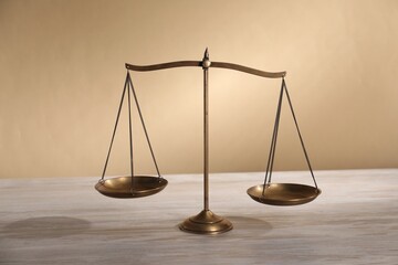 Scales of justice on table against beige background