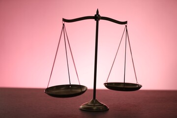 Scales of justice on table against color background