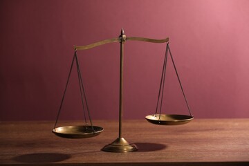 Scales of justice on wooden table against color background