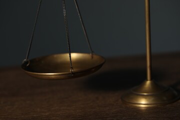 Scales of justice on wooden table against gray background, closeup